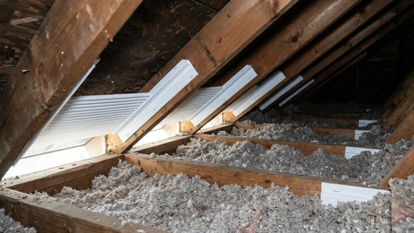 White attic baffles installed between rafters at the eave line, maintaining a clear air channel above blown-in insulation from the soffit vent opening