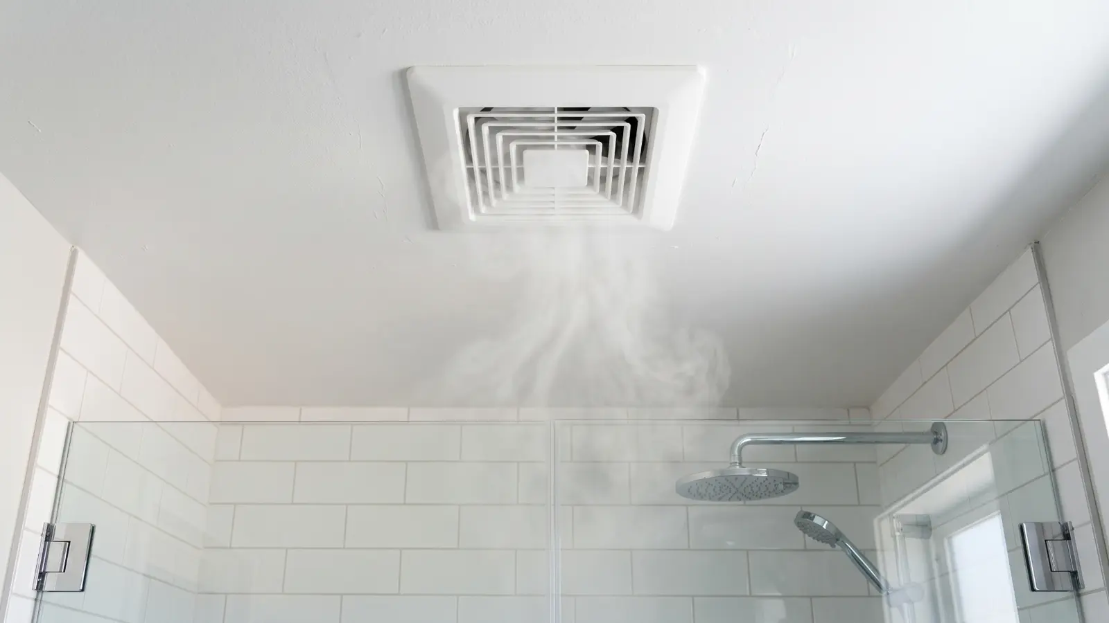 White bathroom exhaust fan mounted on a ceiling above a shower with steam rising toward it