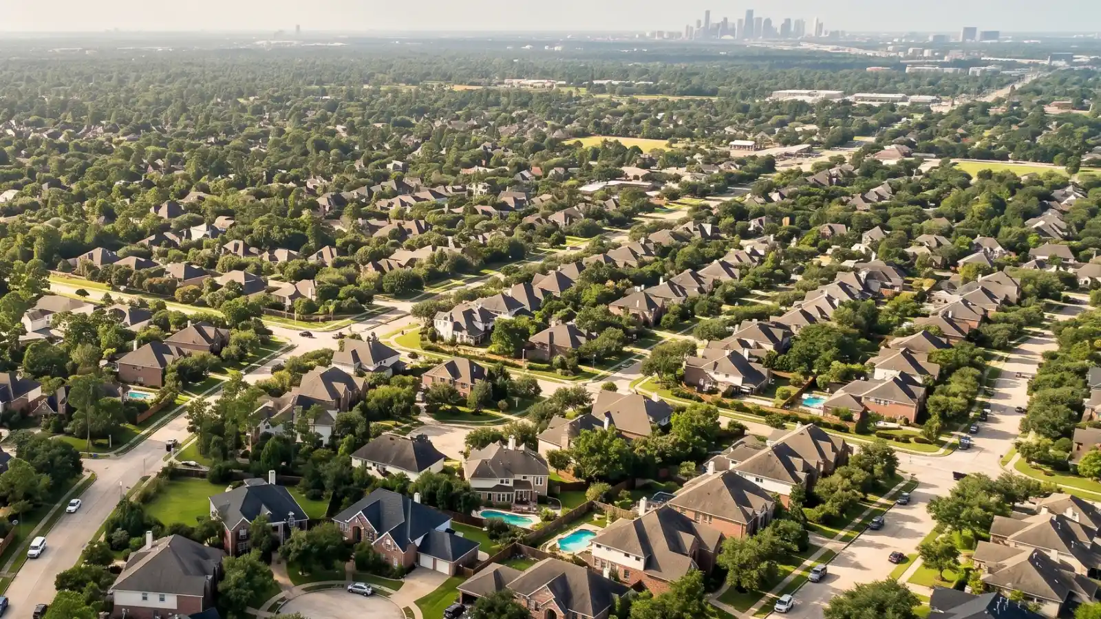 Aerial view of a Houston suburban neighborhood showing large brick homes, tree-lined streets, and the scale of the greater Houston metro area
