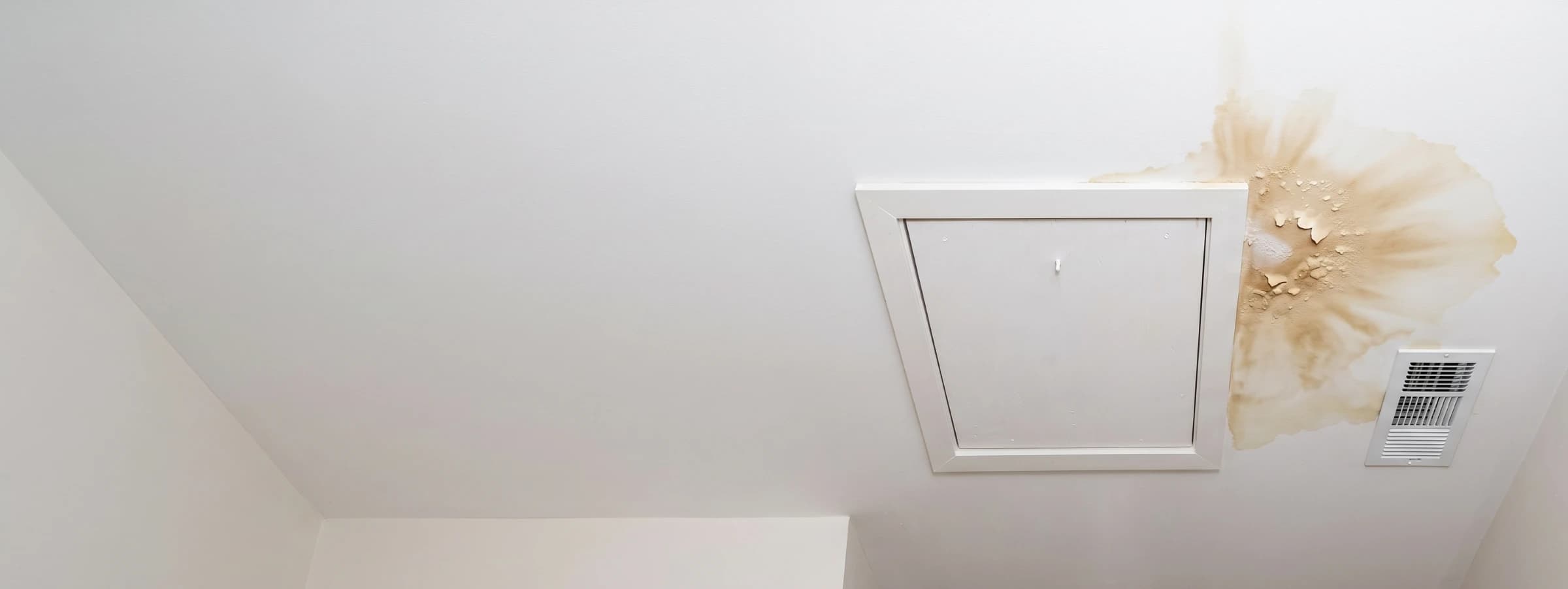 Water stain spreading across a ceiling below an attic HVAC access panel