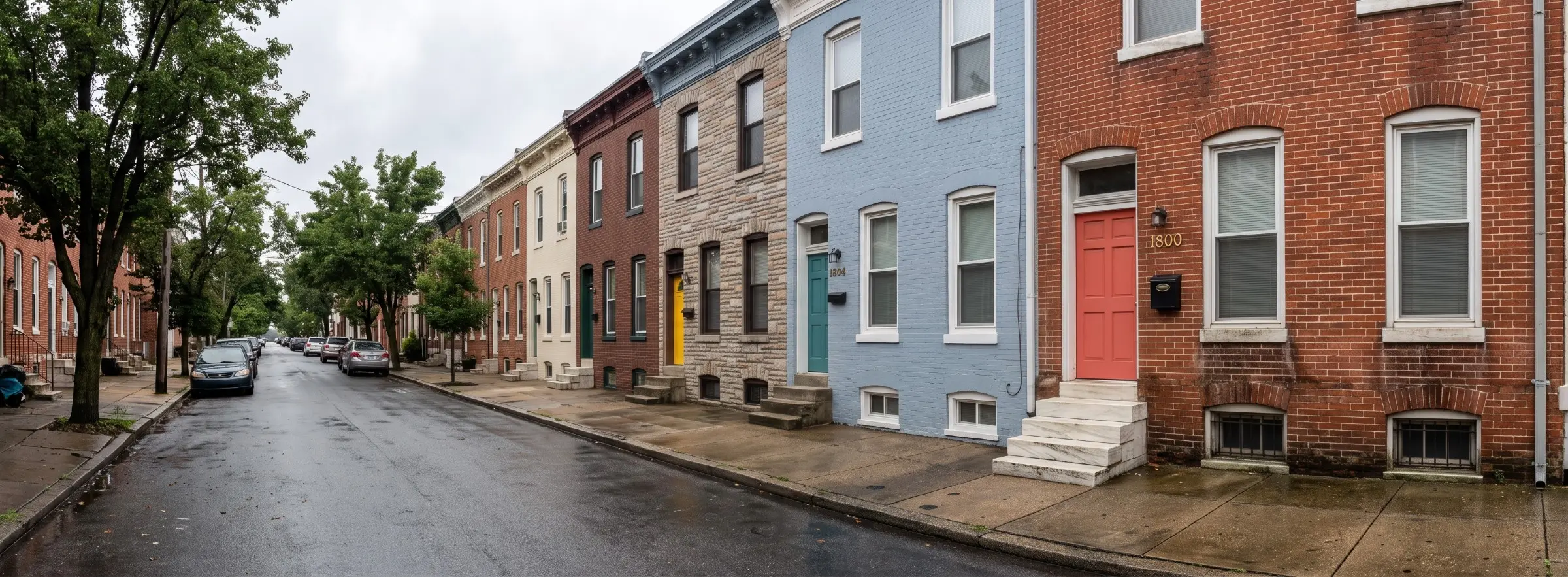 Red brick rowhouse on a wet Baltimore street with damp staining near the foundation